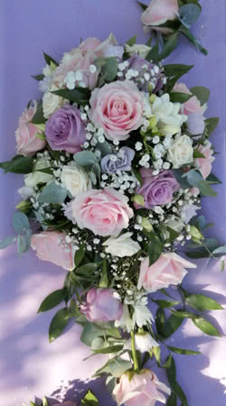 This is a Brides Wedding Bouquet designed in the traditional teardrop style using pink and lilac Roses, Lisianthus, Gypsophila and Ruscus foliage.