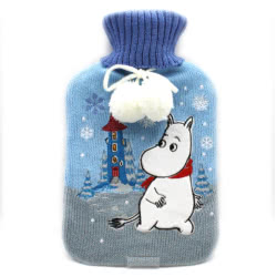 Moomin Snow Hot Water Bottle. This hot water bottle features a knitted cover, with Moomin walking through the winter snow, surrounded by embroidered snow flakes and with Moominhouse in the background. It is finished with fluffy white pompoms.