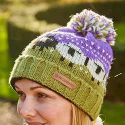 Pachamama Knitwear Black Sheep Roll Back Bobble Beanie Hat Purple features sheep on a green & purple background, 100% Wool, fleece lined