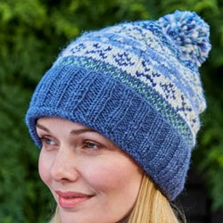Pachamama Knitwear Classic Fairisle Roll Back Bobble Beanie Denim featuring a blue roll back ribbed design, with bands of patterned cream & blue.