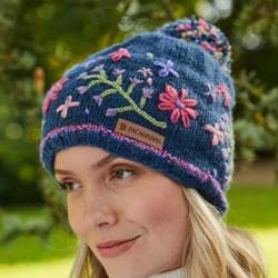 Pachamama Knitwear Hampton Court Hat features blue background with embroidered pink, lilac and green flowers, 100% Wool, fleece lined